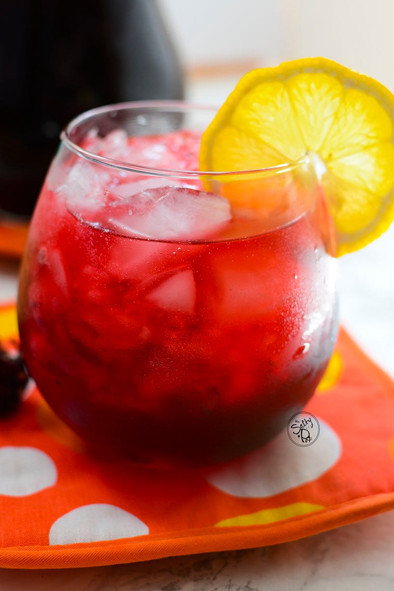 A glass of hibiscus iced tea with ice and lemon.