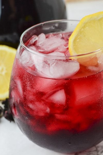 A side view of the iced tea with lemon and hibiscus in the background.