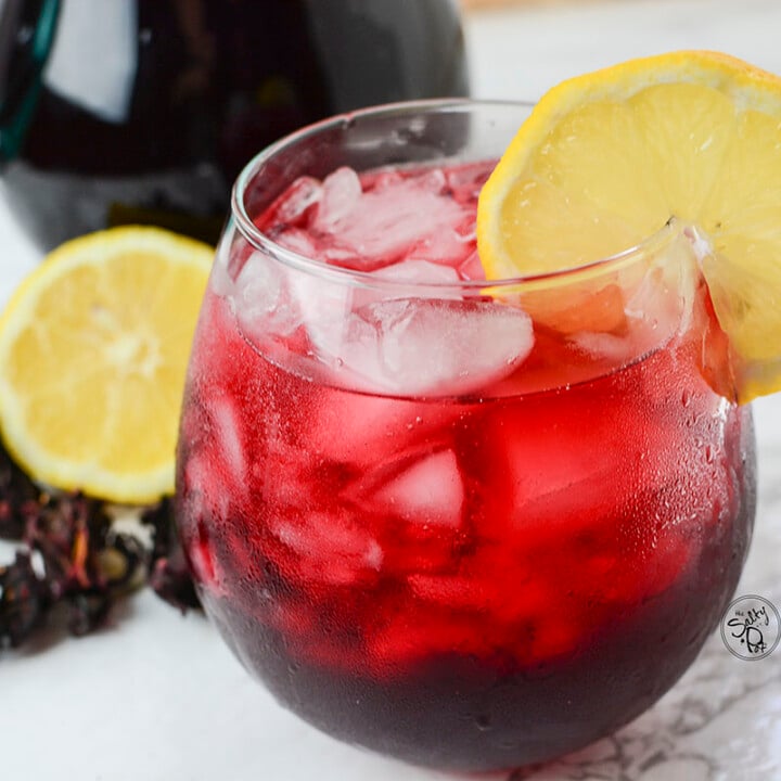 A side view of the iced tea with lemon and hibiscus in the background.