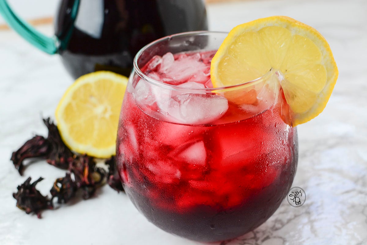 A side view of the iced tea with lemon and hibiscus in the background.