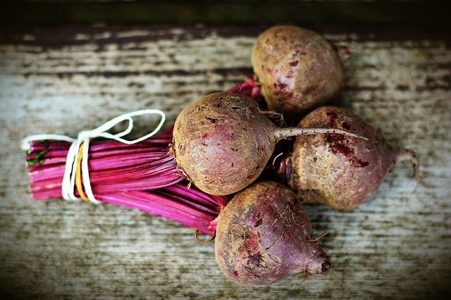 Raw beets sitting on a table with the greens tied with a string.
