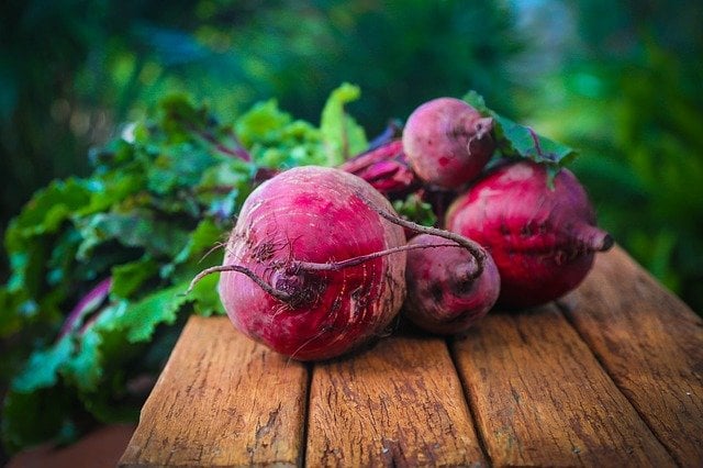 Beets on a wooden table with the greens still attached to the beets. 