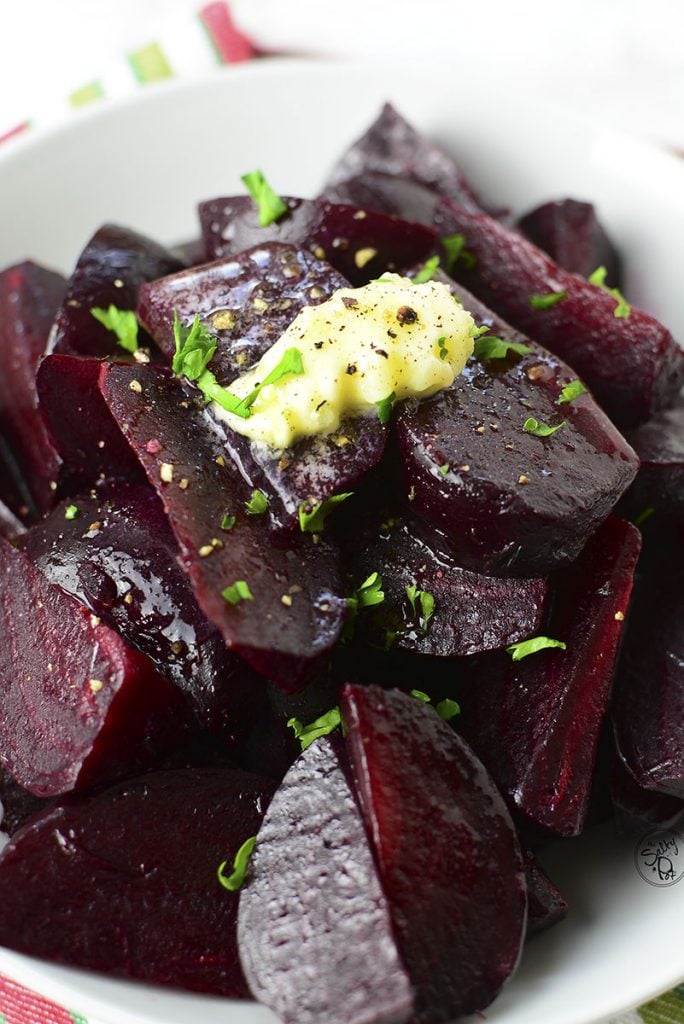 A closeup photo of cooked beets in a white bowl with a dollop of butter melting over the top. 