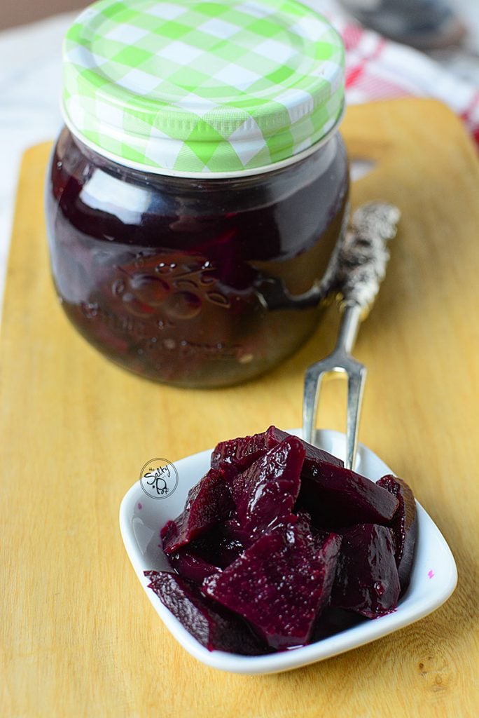 Pickled beets in both a small white bowl and in a canning jar with a white and green lid.