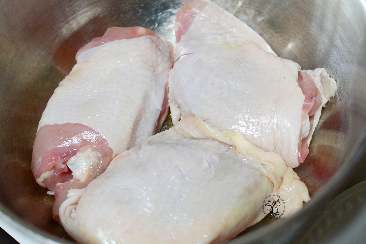 Raw chicken thighs in a silver bowl. 