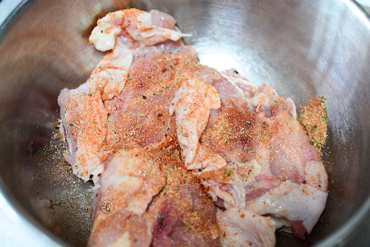 Chicken thighs in a bowl with seasoning over top.