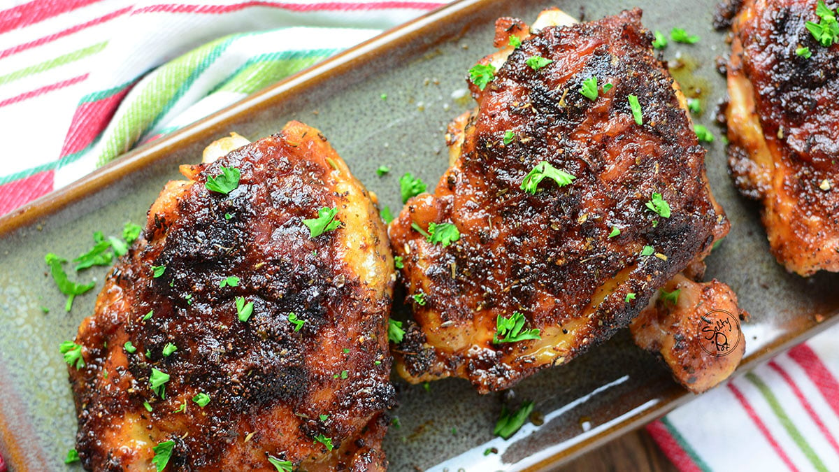 Two chicken thighs on a green ceramic serving plate with a striped napkin beneath.