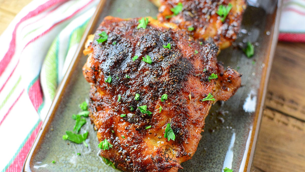 One fully cooked and crispy chicken thigh on a green plate.