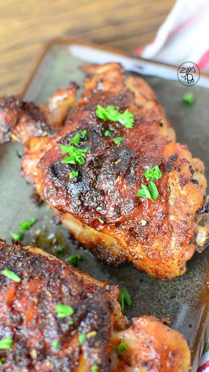 A closeup photo of one chicken thigh with crispy skin. It has flakes of fresh green parsley over top.