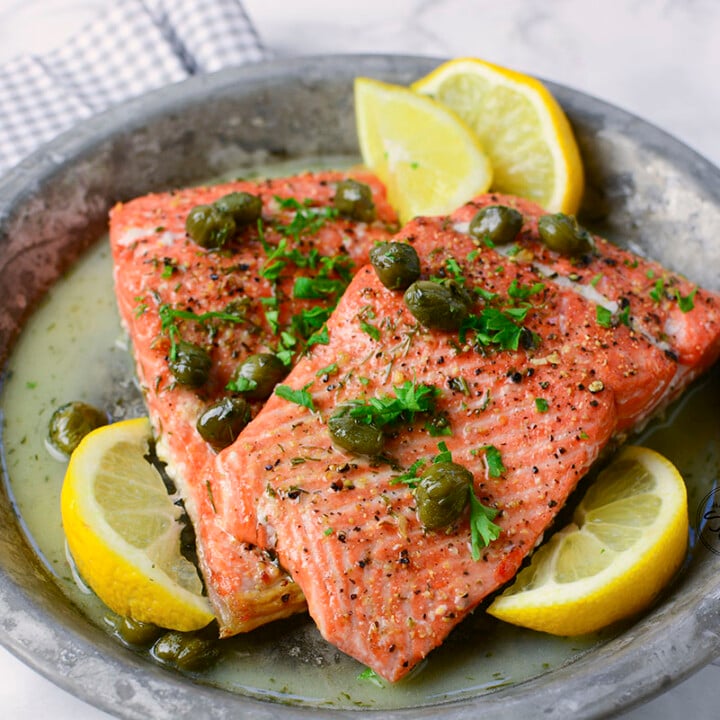 Samon on a plate with lemon wedges and butter sauce.