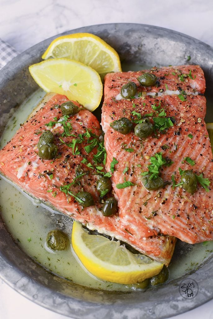 Two pieces of air fryer salmon sitting in a tin plate on a marble background.