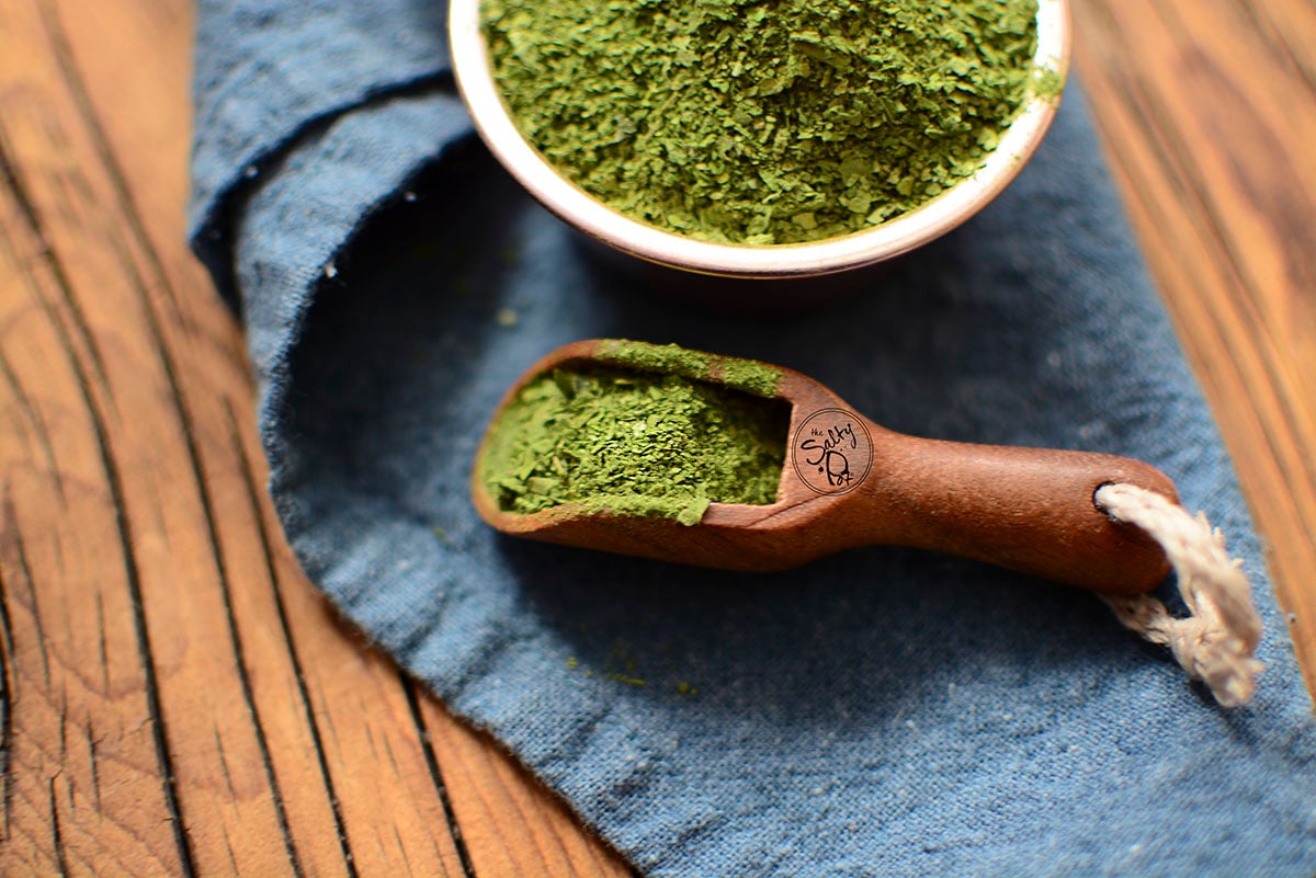 A small wooden scoop spoon holding spinach powder.