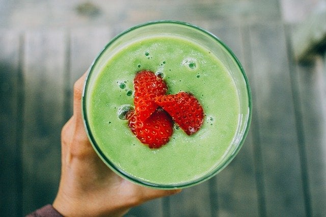 A top down view of a spinach smoothie with cut strawberries on top.