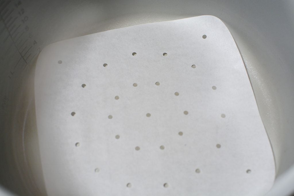 A photo of a parchment paper liner with holes, sitting on the bottom of a ninja foodi. 