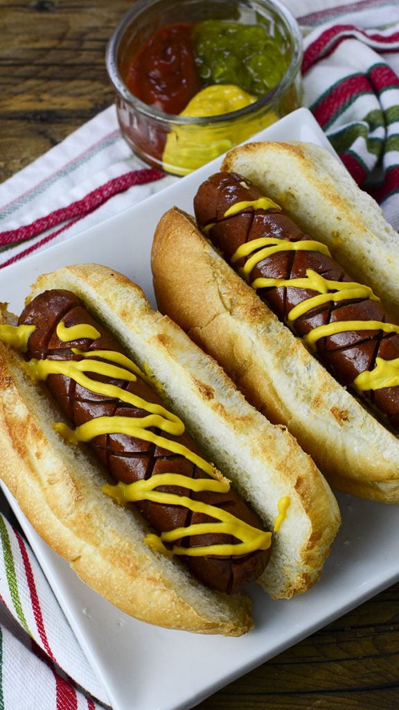 Two air fried hot dogs in buns with mustard drizzled over top.