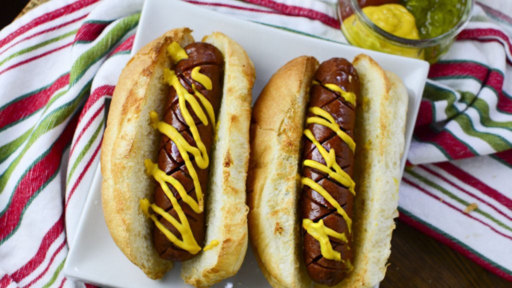 Two air fryer hot dogs in a white plate with a colorful napkin in the background.