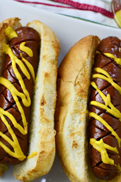 Two air fryer hot dogs in a white plate with a colorful napkin in the background.