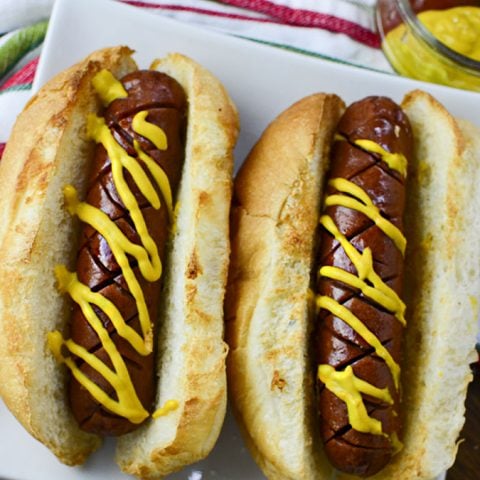 Two air fryer hot dogs in a white plate with a colorful napkin in the background.