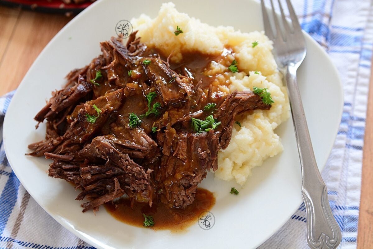Roast beef with mashed potatoes with a fork on the plate on the right side. 