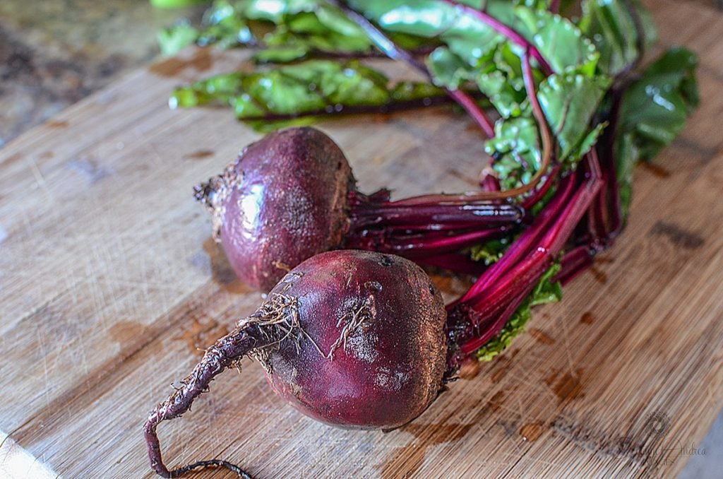 Two beets with greens still attached, sitting on a wooden cutting board.