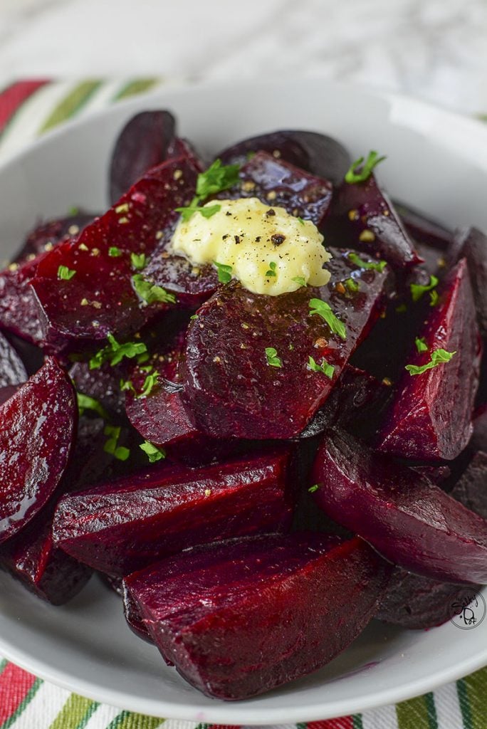 Ruby red pressure cooked beets sitting in a white bowl on a colorful napkin.