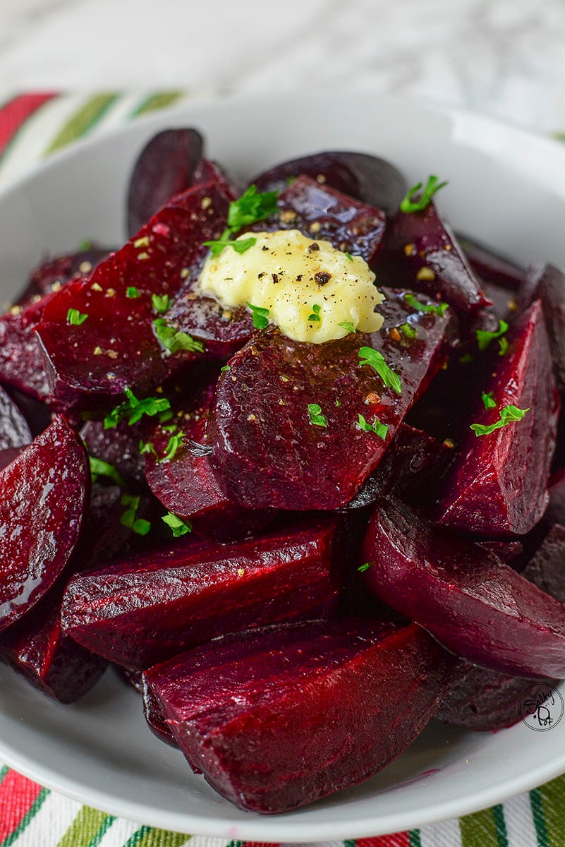 Ruby red pressure cooked beets sitting in a white bowl on a colorful napkin.