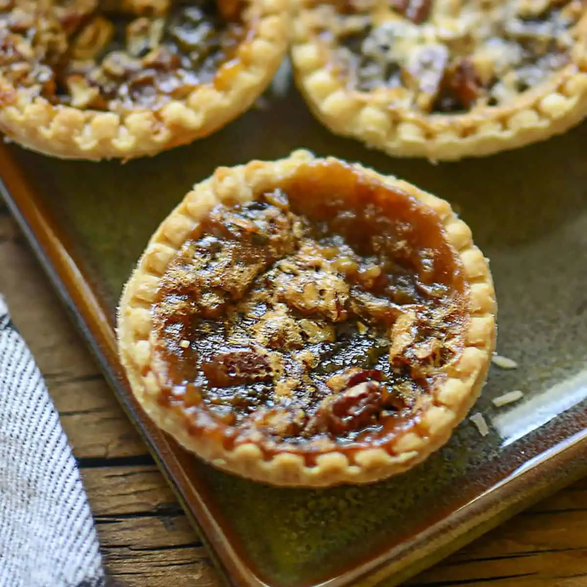 One butter tart shown close up with two other ones in the background at the top.