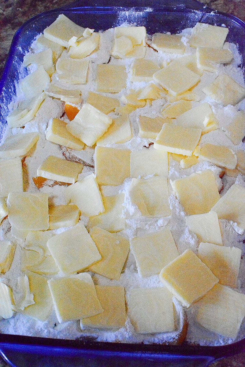 Cold butter placed on top of the dry cake mix in a blue baking dish.