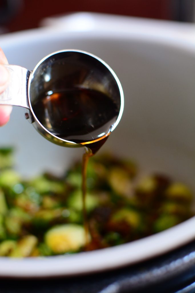 Drizzling in the maple syrup to the cooked sprouts from a silver measuring cup.