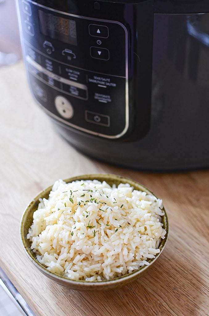 A bowl of pressure cooked rice sitting in the forefront with the Ninja Foodi in behind.