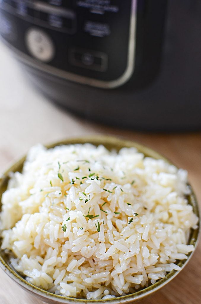 A close up photo of cooked rice in a green bowl with a sprinkle of parsley over top.