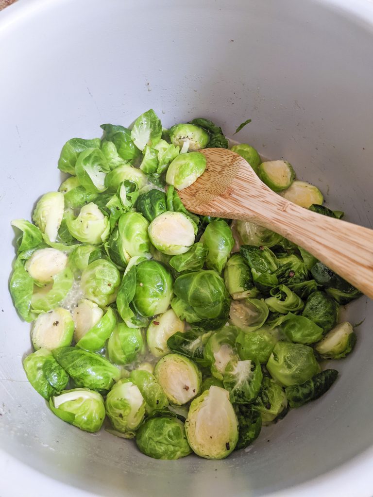 Sauteed brussel sprouts with a wooden spoon on the top right side.