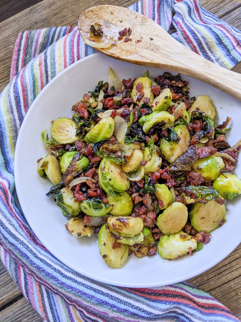Brussel sprouts sitting on a white plate with a wooden spoon on the top right side. 