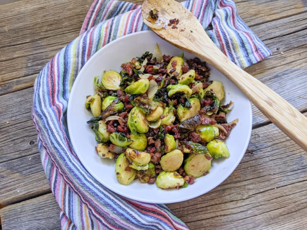 Air fryer brussels sprouts in a white bowl with a wooden spoon resting on the edge.