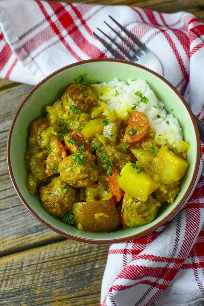 Slow cooker sausage curry in a green bow on a wooden backdrop.