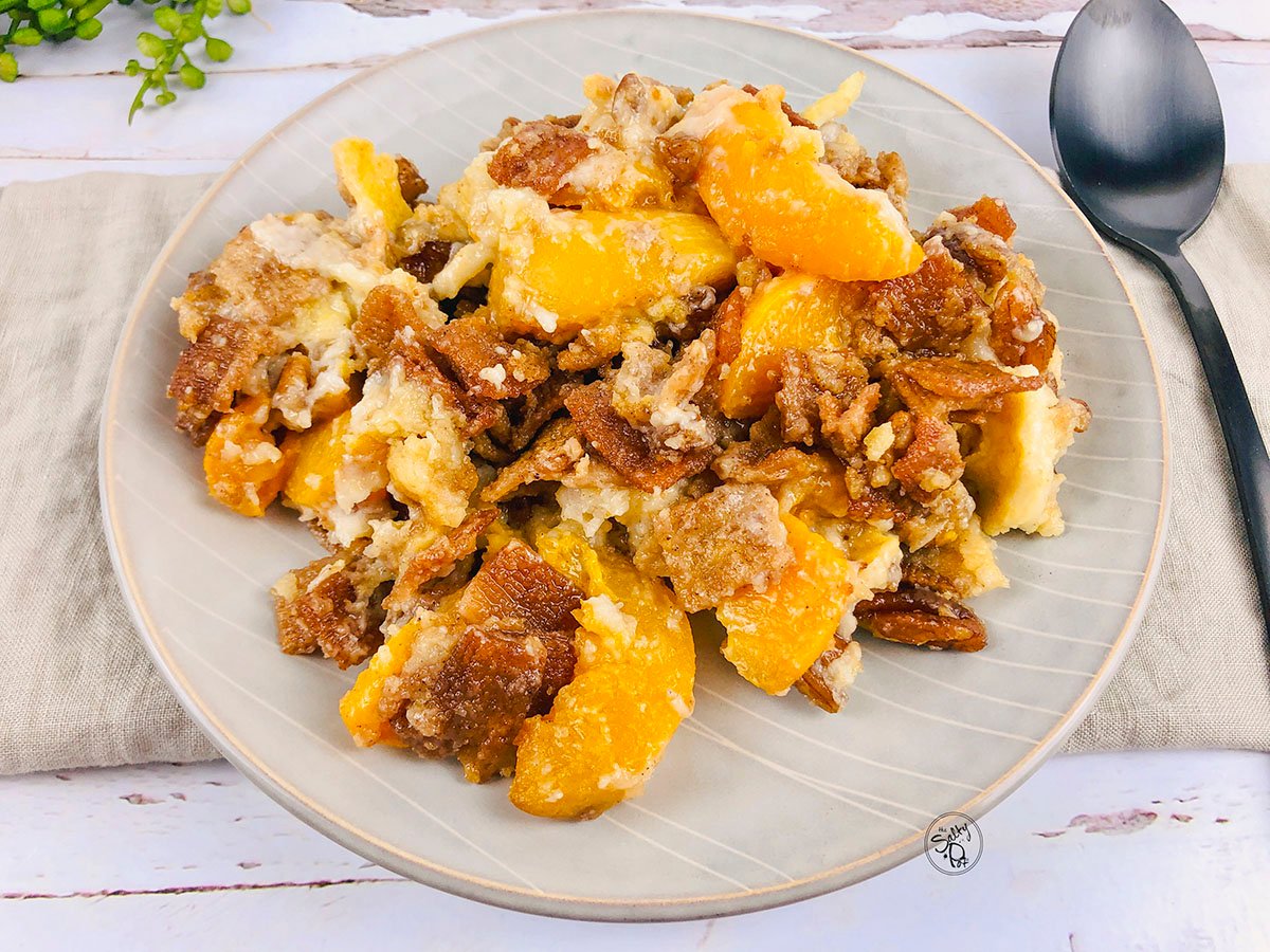 A horizontal photo of the peach dessert on a beige plate with a spoon on the right.