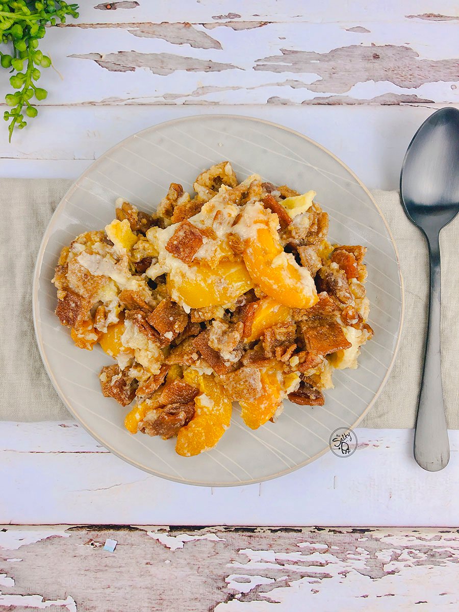 Peach cobbler on a beighe plate with a spoon on the right.