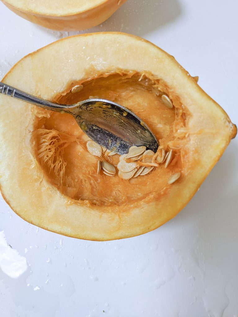 A spoon inside the center of the squash, cleaning out the strands and seeds.