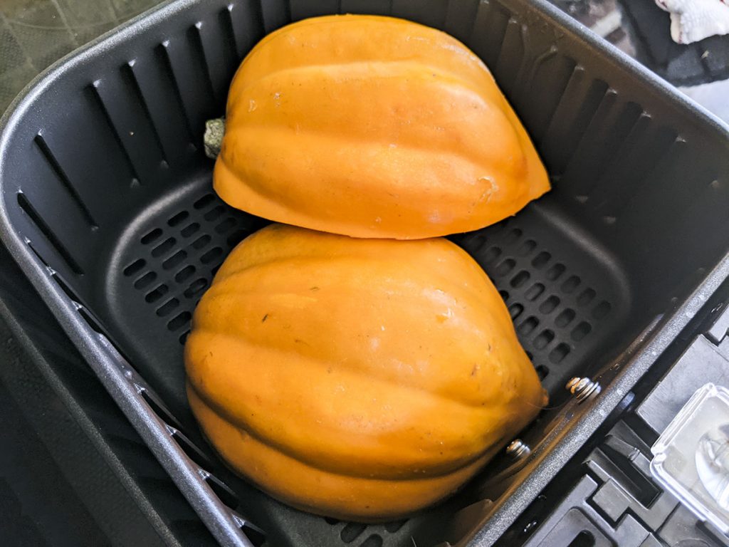 Two halves of an acorn squash sitting cut side down in the air fryer, ready to be cooked.
