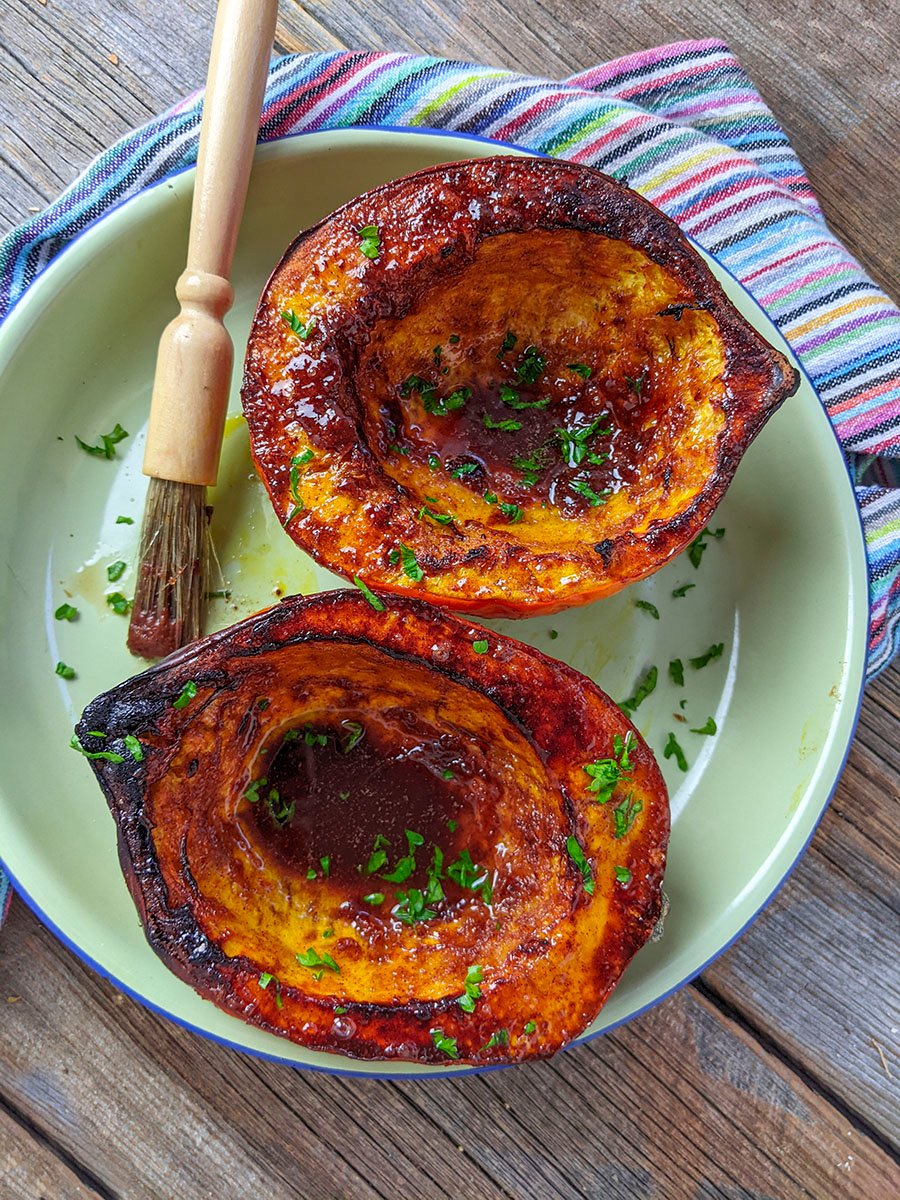 Two halves of an acorn squash that's been air fried sitting on a green plate with a pastry brush beside it.