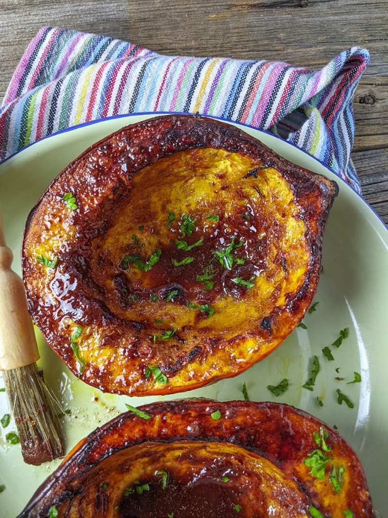 One half of the acorn squash sitting with the pastry bruch beside it on a green plate and a multicolored napkin.