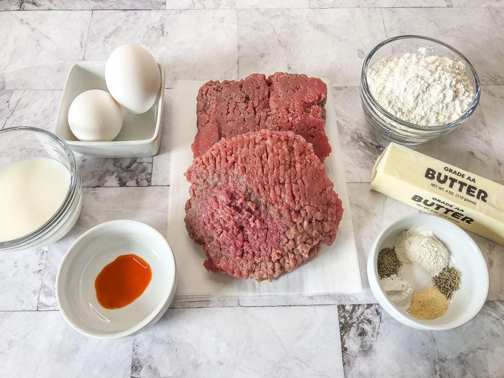 The ingredients needed to make this recipe are gathered together. The cube steak is sitting on a plate in the center.