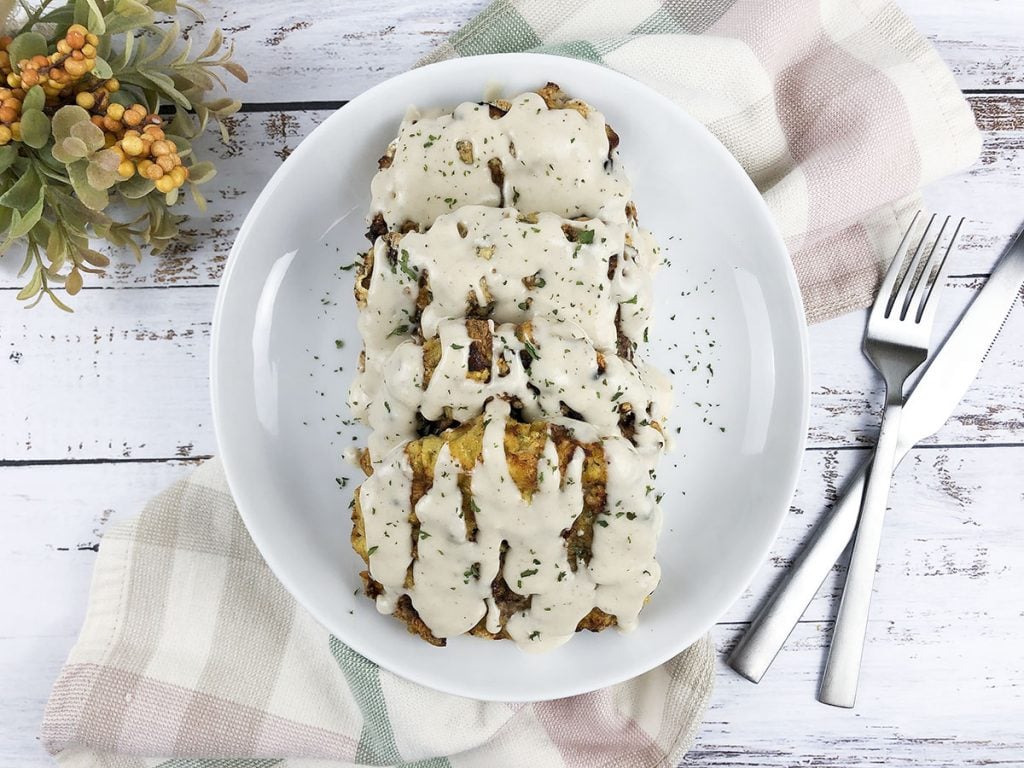 3 air fryer chicken fried steaks sitting on a white plate with a savory white gravy poured on them. 