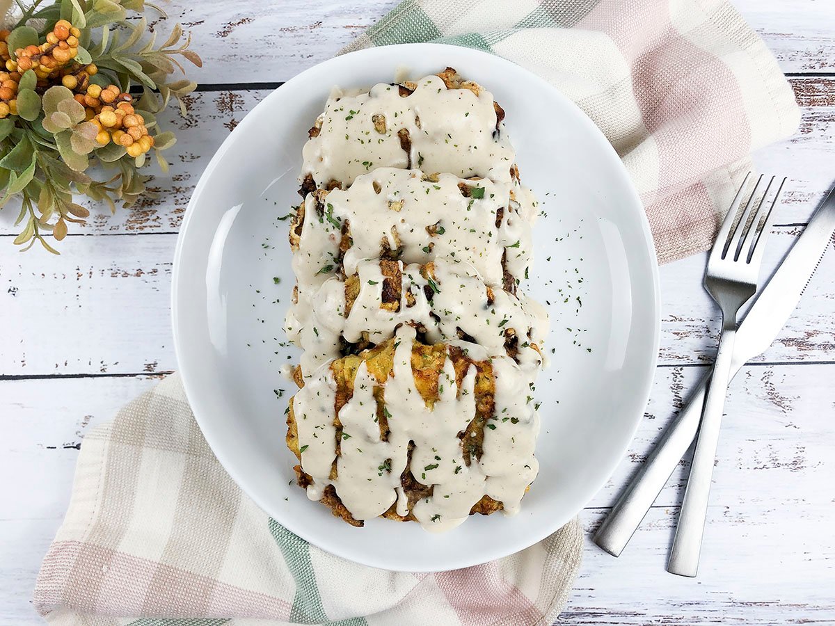 3 peices of delicious air fryer chicken fried steak on a white plate, with gravy poured over top.