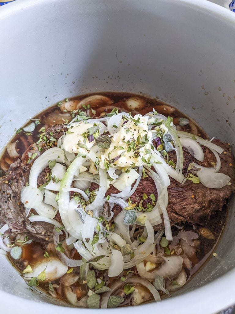 The roast is ready to pressure cook with onions, garlic, butter and thyme sitting on top of it. 