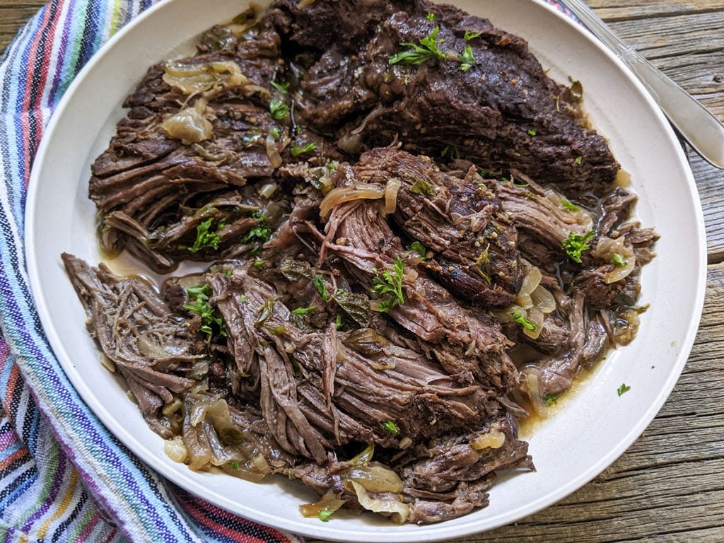 Pressure cooked beef roast on a white plate with a colorful napkin on the left.