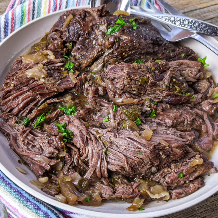 A pressure cooked beef roast on a wood background with a colorful napkin on the left side.