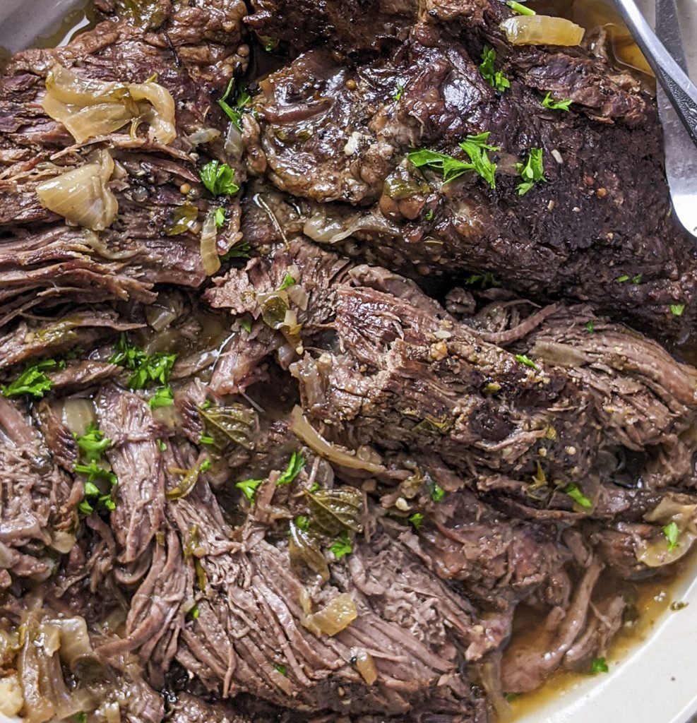 A super close up photo of the roast. Onions and green parsley are sprinkled over the top.