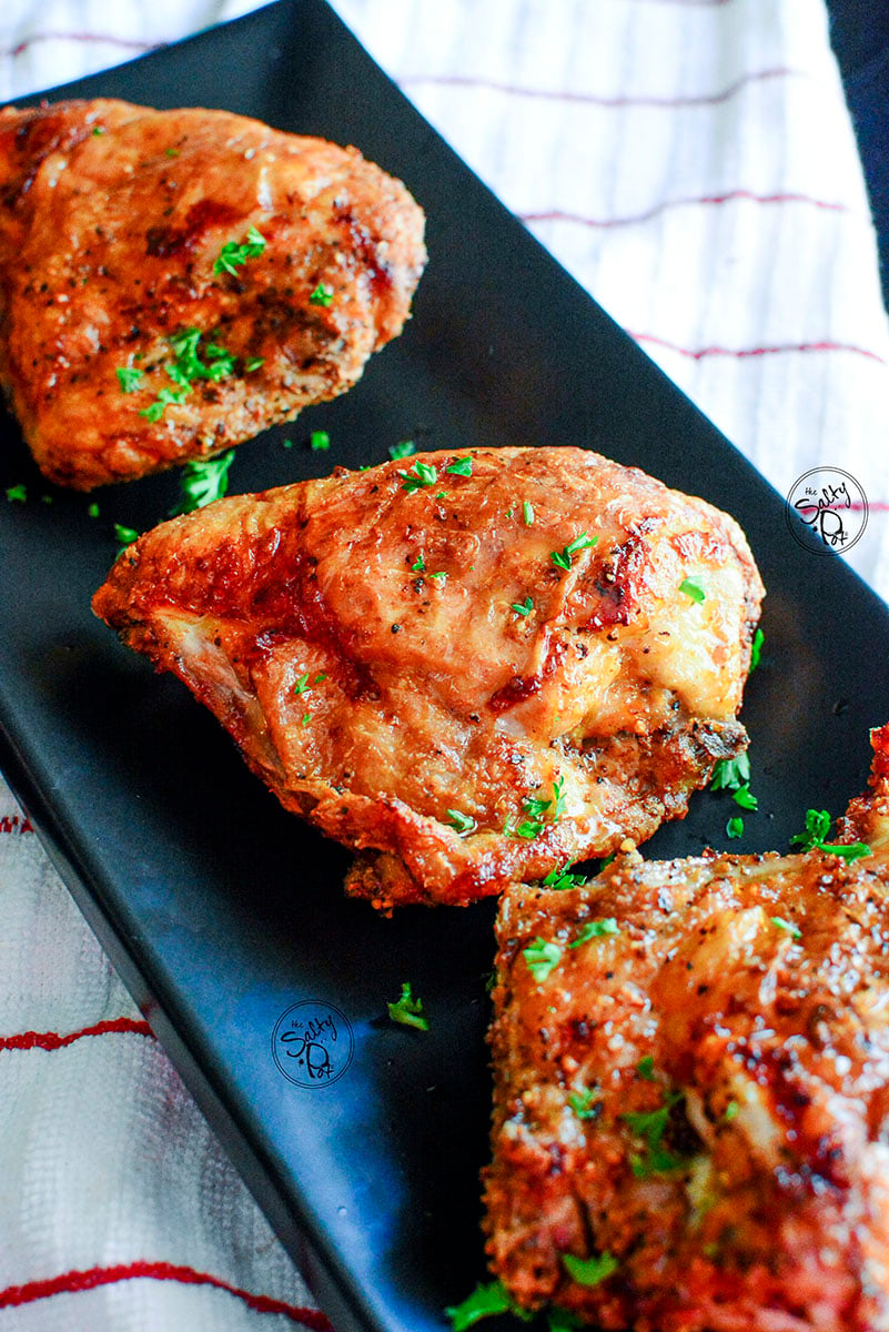 A close up photo of two air fried bone in chicken breasts with crispy skin on a long black plate.