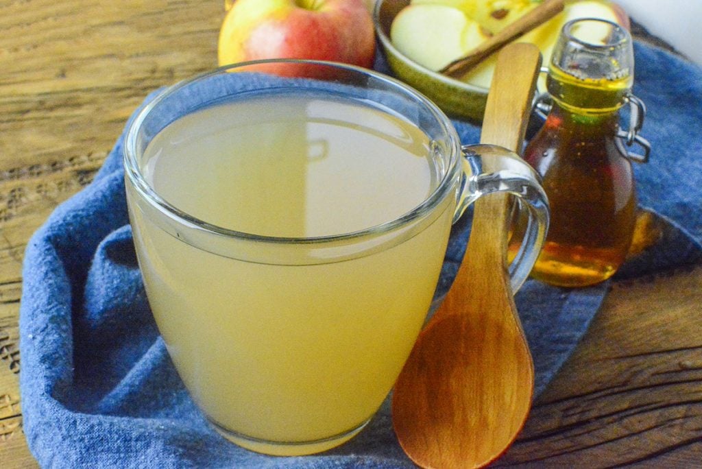 Homemade apple cider in a clear mug with a wooden spoon through the handle.
